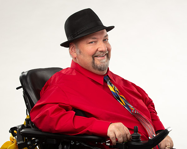 Dave in his wheelchair wearing a red shirt and multicolored tie.
